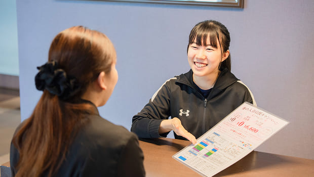 ジムの受付でトレーナーから説明を受ける女性の写真