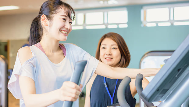 女性トレーナーに見守られながらトレーニングジムを体験している女性の写真