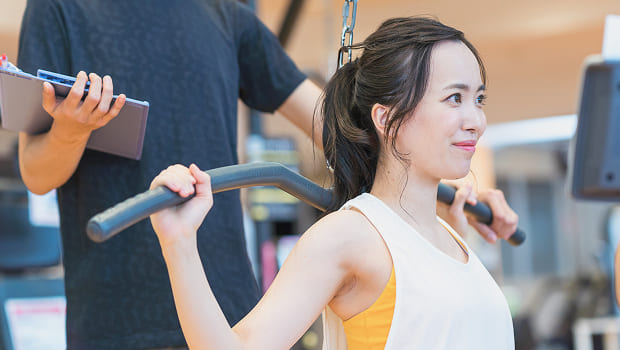 マシンを使ってトレーナーにマンツーマンでトレーニングを受ける女性の写真